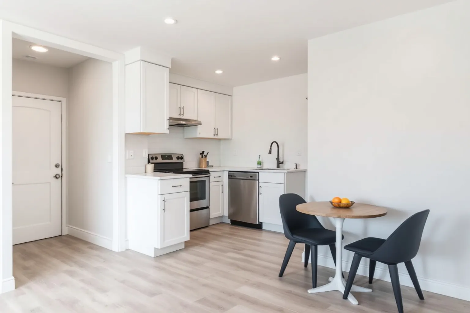 Example of a Brampton basement suite with a small white kitchen, stainless range and dishwasher, a round table with two dark chairs and a separate entry door