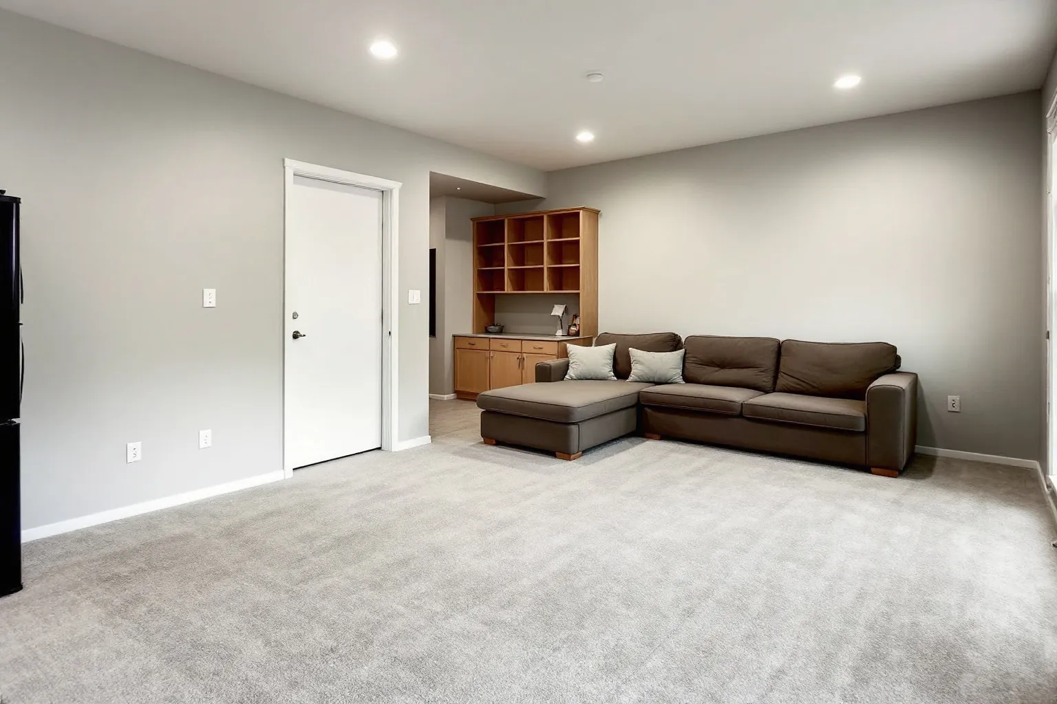 Example of a finished Pickering basement with grey carpet, a brown sectional sofa, pot lights, a white door and a built in oak shelf and desk