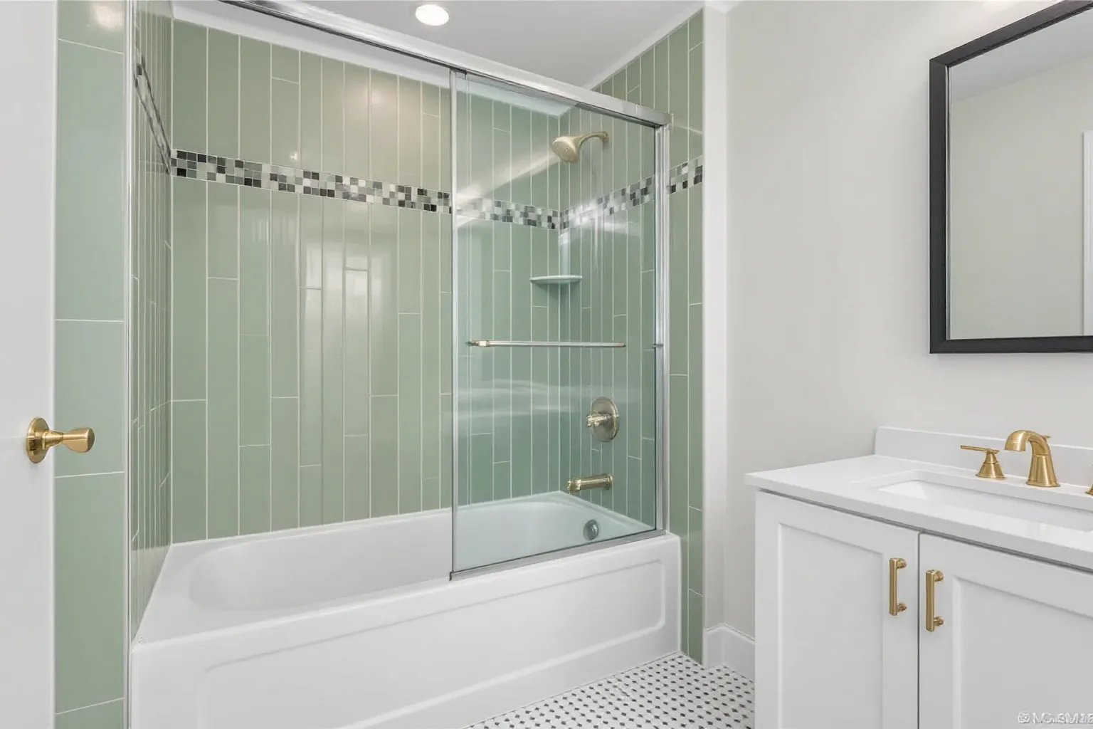 Example bathroom with sage green tile, a tub with a glass panel and a white vanity with brass handles