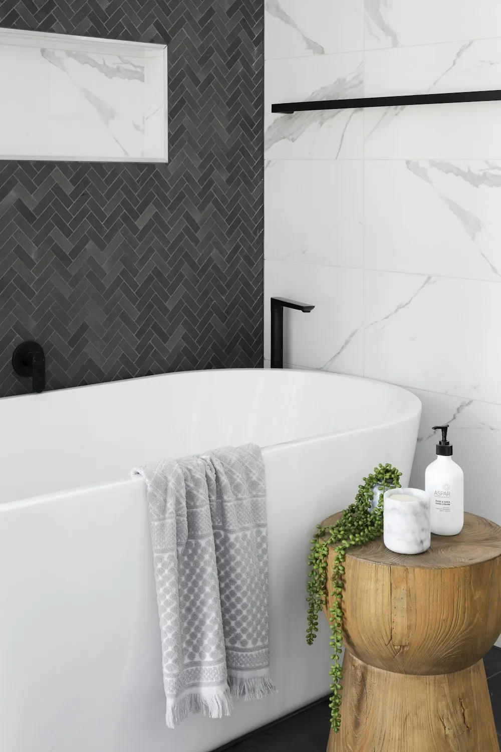 Bathroom with a dark herringbone tile wall and a freestanding white tub