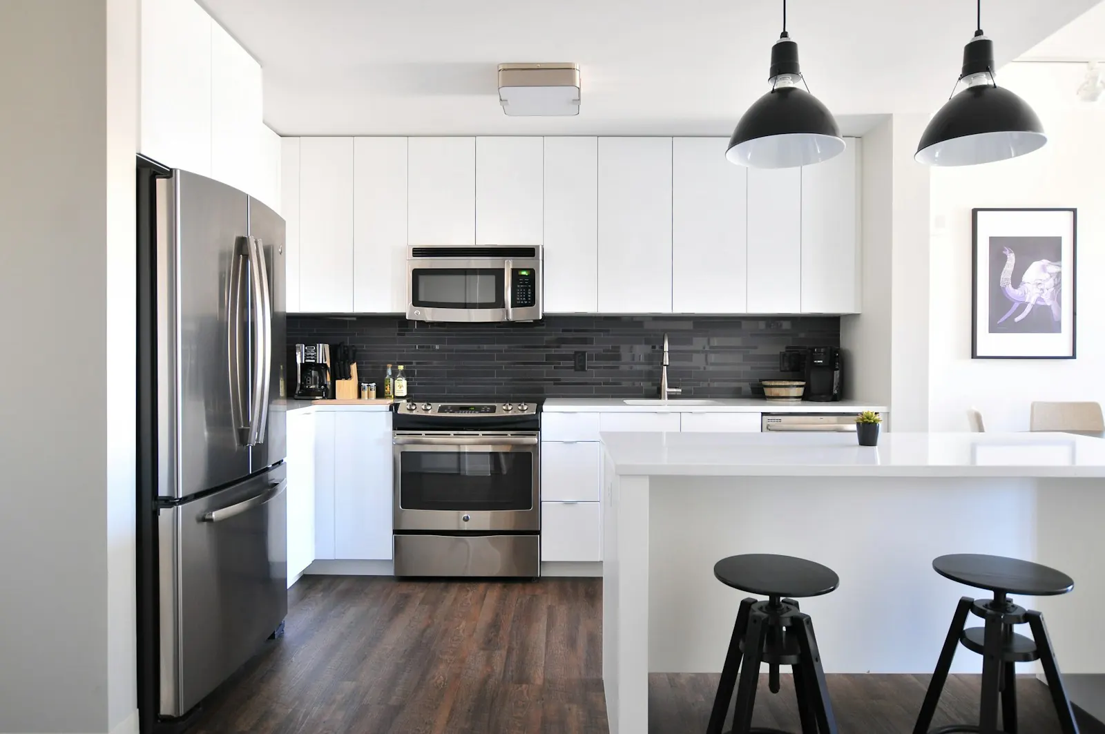 White kitchen with a dark tile backsplash, island and two black stools
