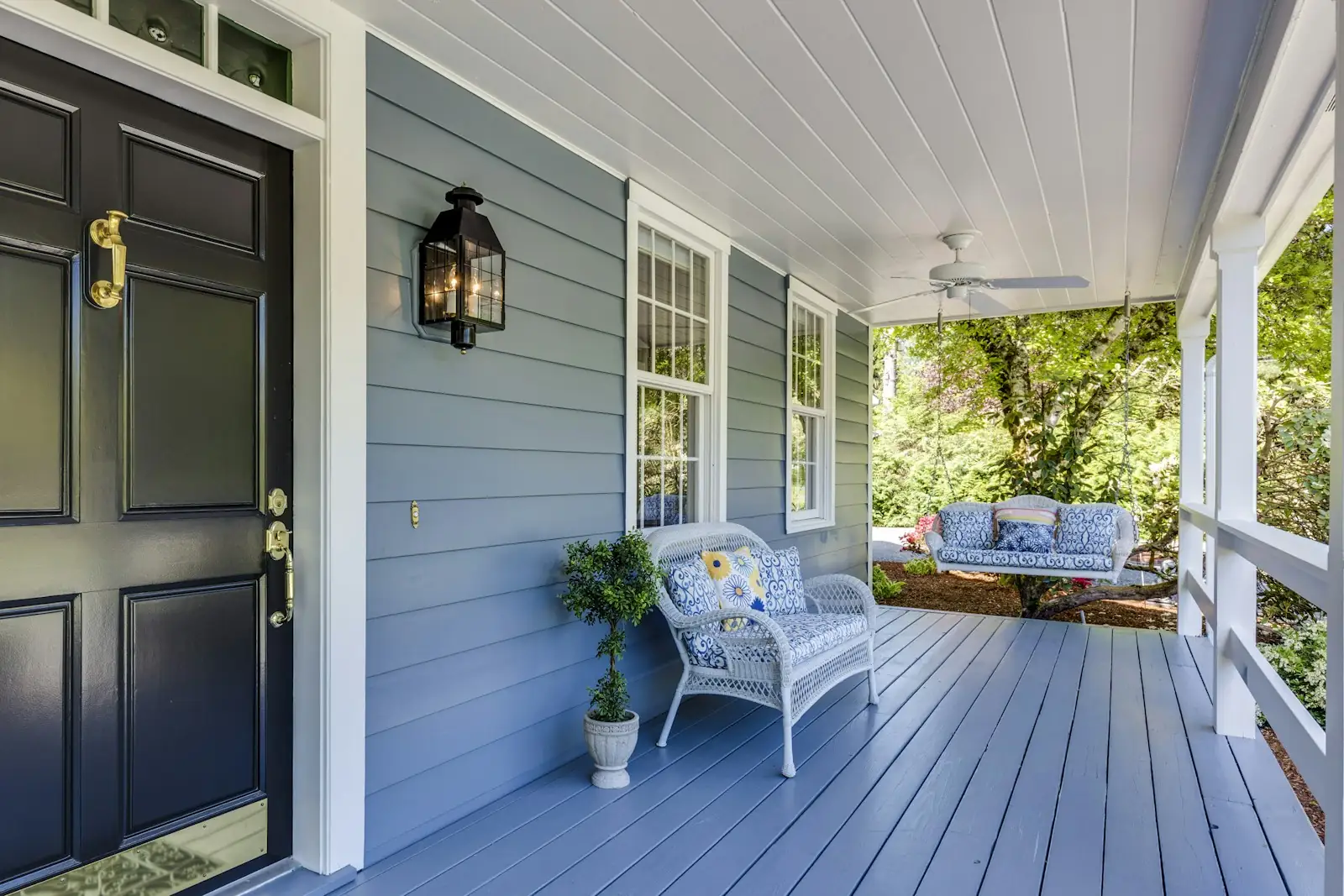 Covered front porch with new blue siding, a black door and a wicker chair